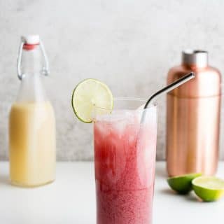 Refreshing Cape Cod Cooler cocktail with lime slice and metal straw with copper cocktail shaker and homemade orgeat syrup