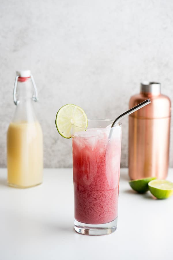 Refreshing Cape Cod Cooler cocktail with lime slice and metal straw with copper cocktail shaker and homemade orgeat syrup