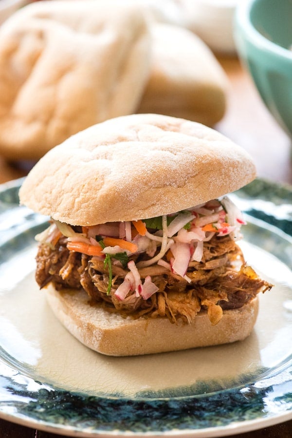 Juicy, tangy slow cooker pulled pork sandwich with radish slaw and gluten-free white roll on green plate