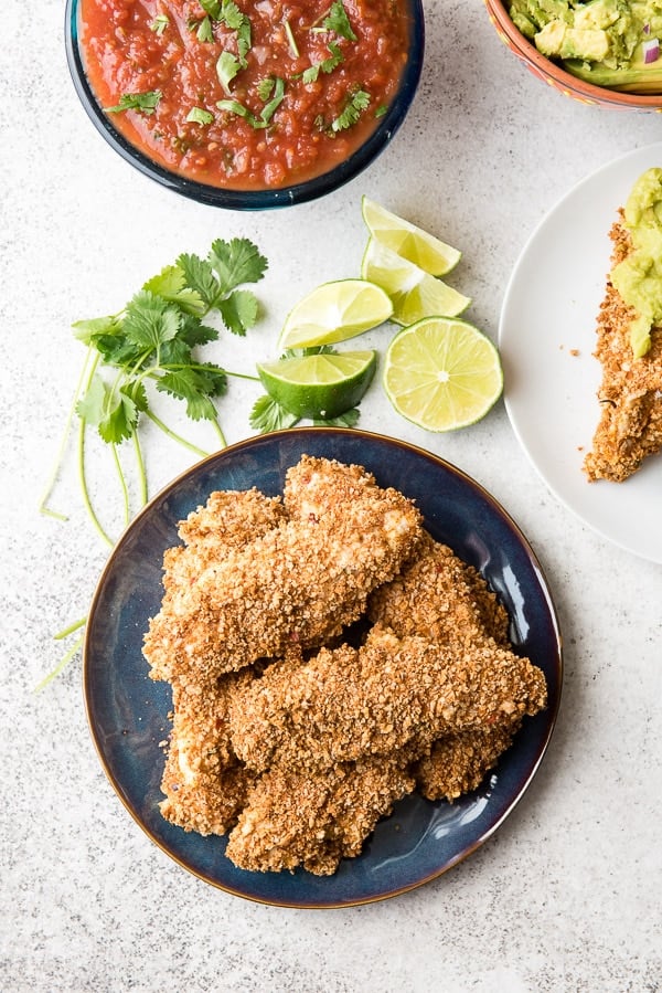 Crunchy, freshly baked Taco Chicken Tenders on a blue plate with lime slices, cilantro