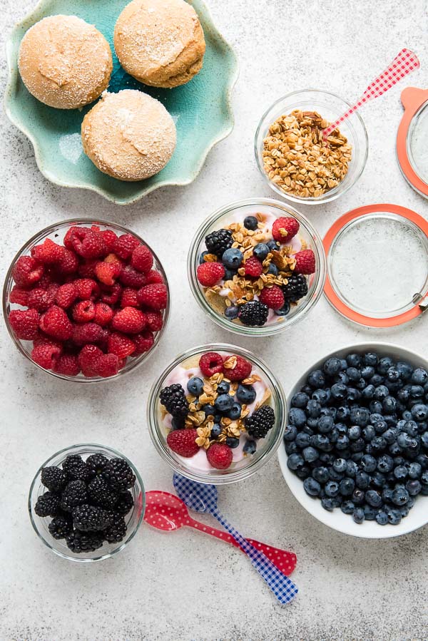 Jars of freshly prepared Overnight Lemon Muffin Breakfast Trifles with bowls of fresh raspberries, blueberries