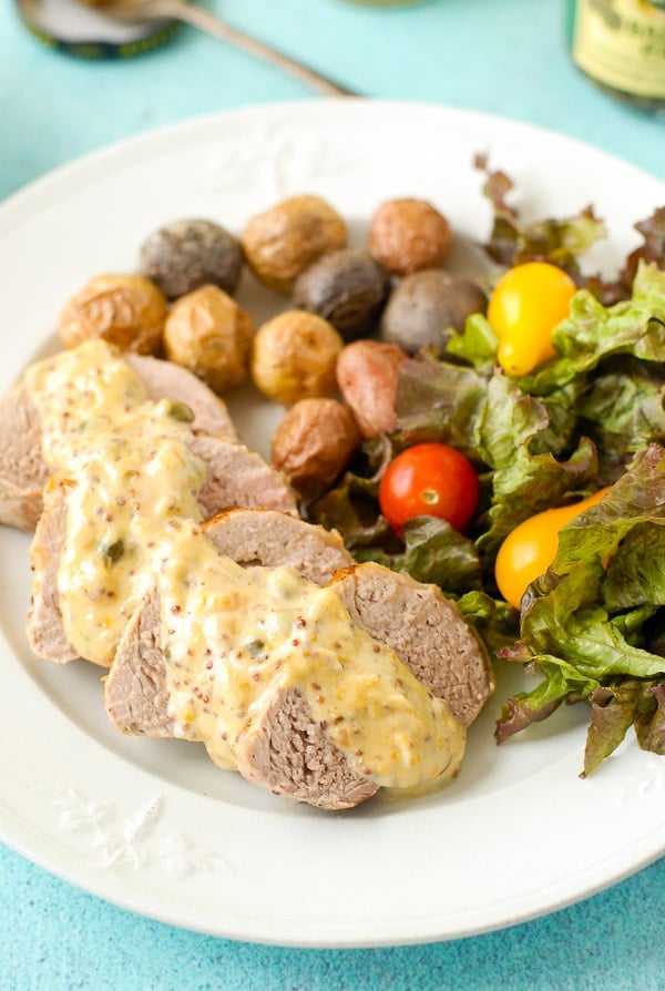 Slices of Pork Tenderloin with Mustard Caper Cream Sauce, fresh salad and roasted potatoes on a vintage ironstone plate