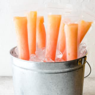 Frosty orange and pink Tequila Sunrise Freezer Pops in a galvanized bucket of ice