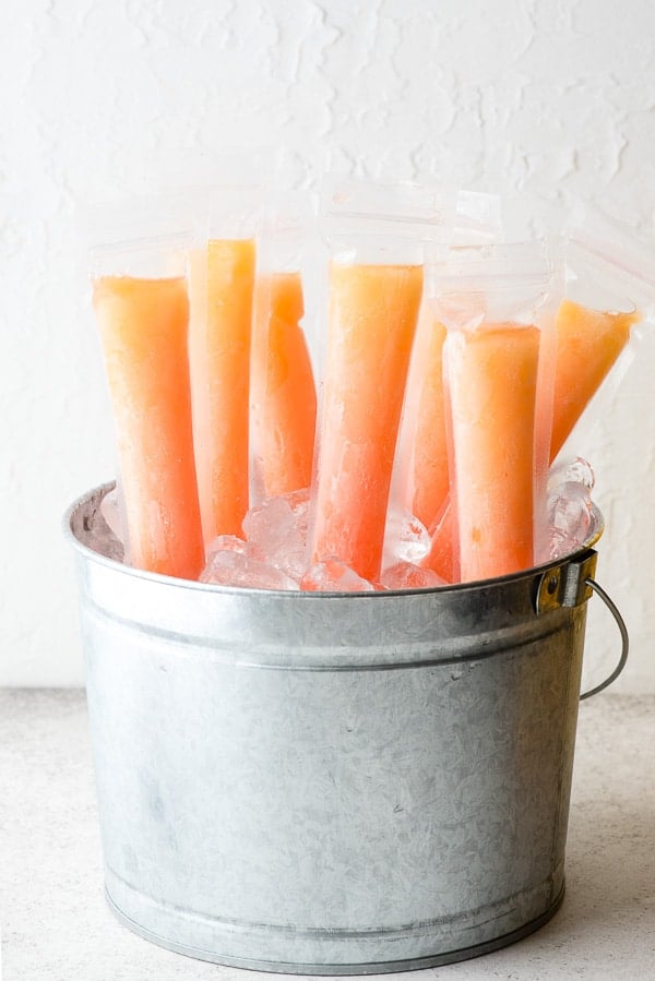 Frosty orange and pink Tequila Sunrise Freezer Pops in a galvanized bucket of ice