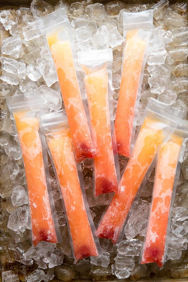 Frosty orange cocktail Tequila Sunrise Freezer Pops with maraschino cherries on a tray of ice