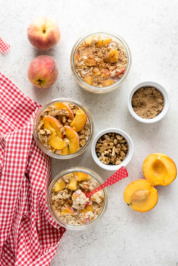 Individual servings of gluten-free Peach Pie Overnight Oats in glass jars with sliced peaches