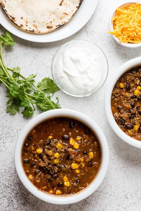 Southwestern Instant Pot Chili with charred corn tortillas, sour cream and cilantro in white soup bowls 