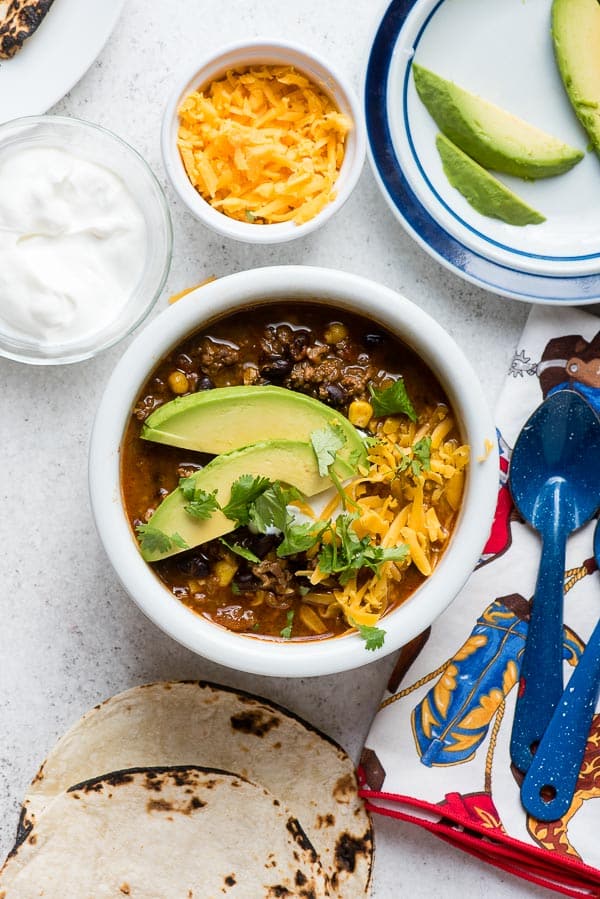 White bowl of Instant Pot Chili with avocado sliced and shredded cheese