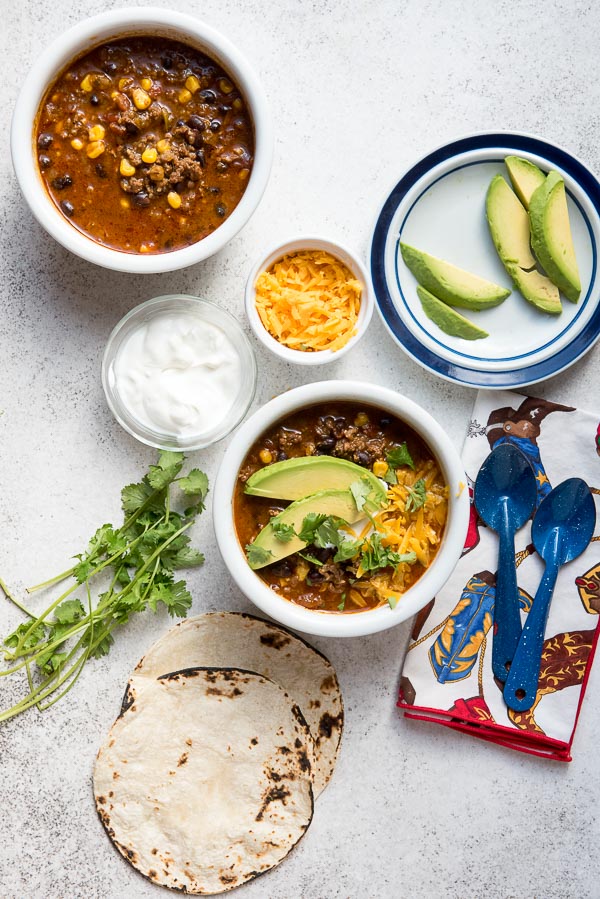 White bowls of steamy hot Instant Pot Southwest Chili with sour cream, cheese, avocados, charred tortillas 