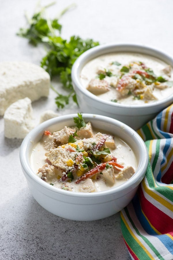 Two white bowls Jalapeno Corn Chicken Chowder with fresh cilantro, crumbled cojito cheese