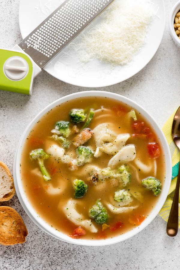 Single serving of gluten-free Pesto Tortellini soup in a white porcelain bowl with finely grated Parmesan cheese 