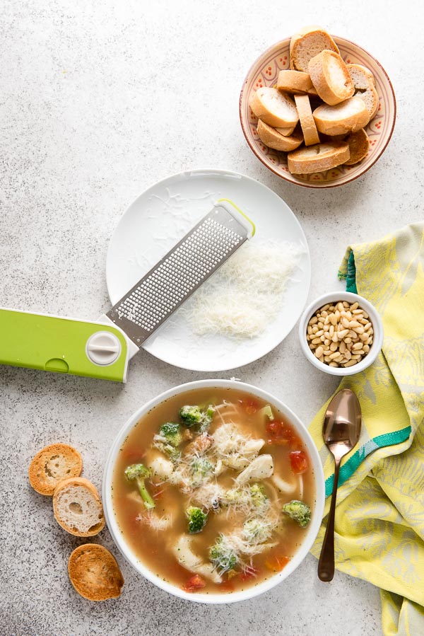 White bowl of gluten-free Pesto Tortellini soup with finely grated Parmesan cheese