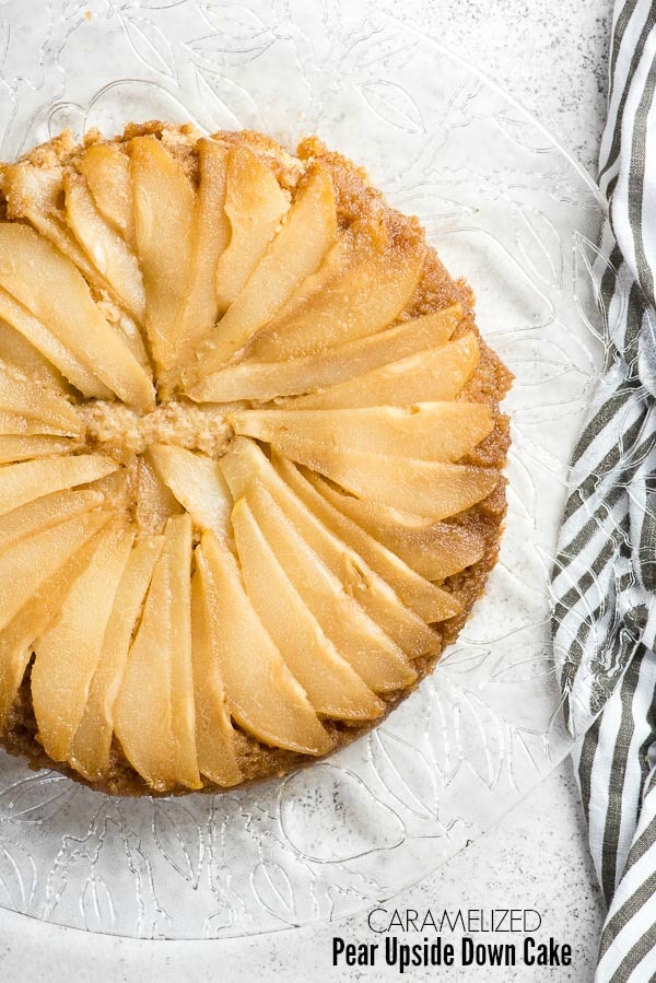 Caramelized Pear Upide Down Cake on a glass etched platter with black and white striped cloth napkin