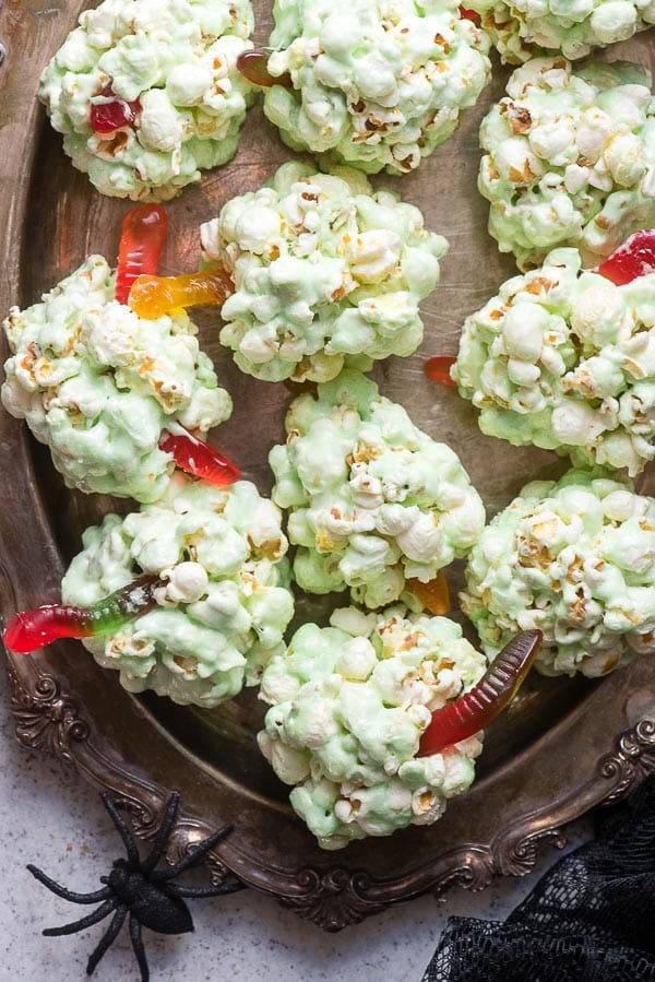 Green Fast Easy Popcorn Balls for Halloween with gummy worms on an antique silver tray with spiders