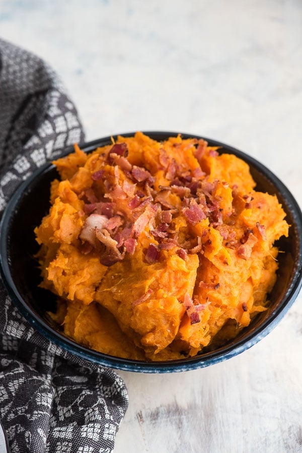 Creamy bowl of Instant Pot Mashed Chipotle Sweet Potatoes in a black glazed bowl with gray kitchen towel 