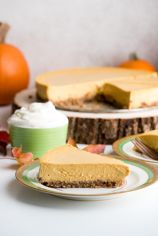 Slice of creamy Pumpkin Cheesecake with oat pecan crust, whipped cream and fall leaves 