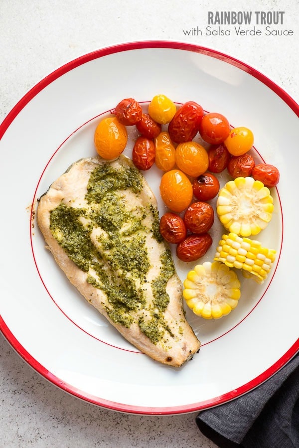 : Rainbow Trout with Salsa Verde Sauce, blistered cherry tomatoes and fresh corn wheels on a white enamel plate