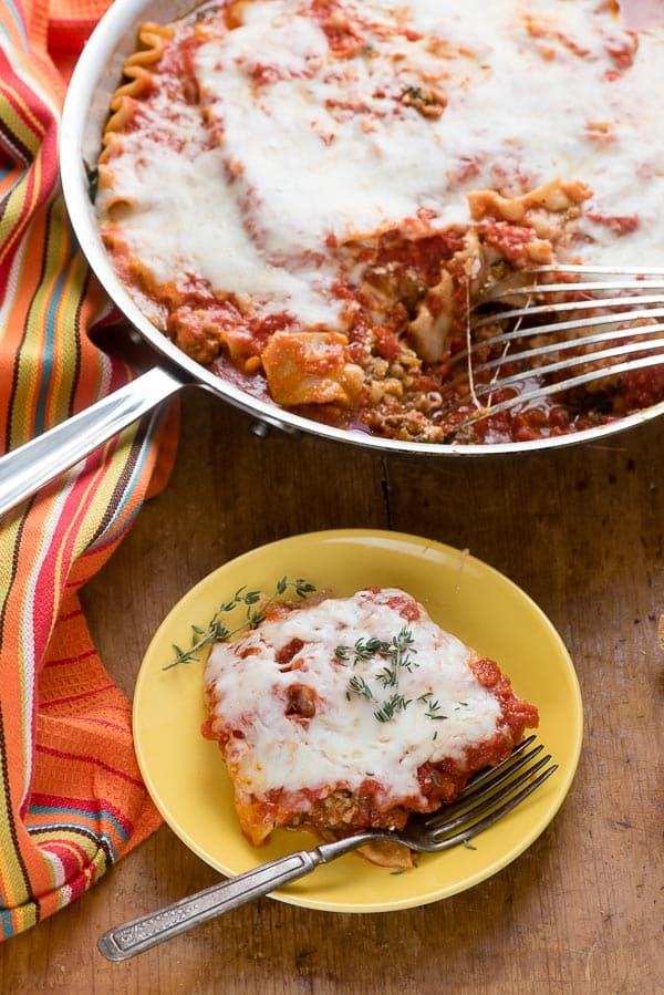 Single slice Spicy Sausage Skillet Lasagna on yellow plate with silver fork, with skillet 