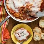 Spicy Sausage Skillet Lasagna with melted cheese top, single serving on small yellow plate with sliced gluten-free baguette