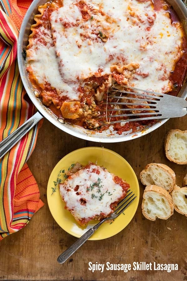 Spicy Sausage Skillet Lasagna with melted cheese top, single serving on small yellow plate with sliced gluten-free baguette 