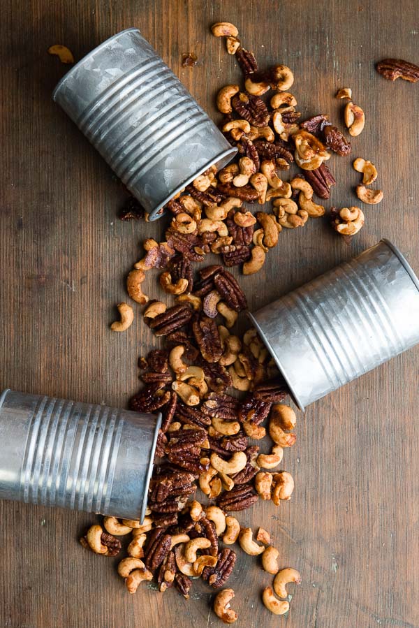 Three galvanized cans tipped over spilling Sweet Spiced Nuts over a dark wood antique bread 