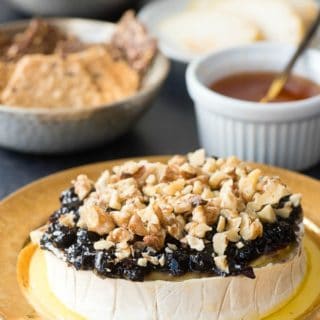 Blueberry Walnut Baked Brie with drizzled honey on an antique gold rimmed plate with gluten-free crackers