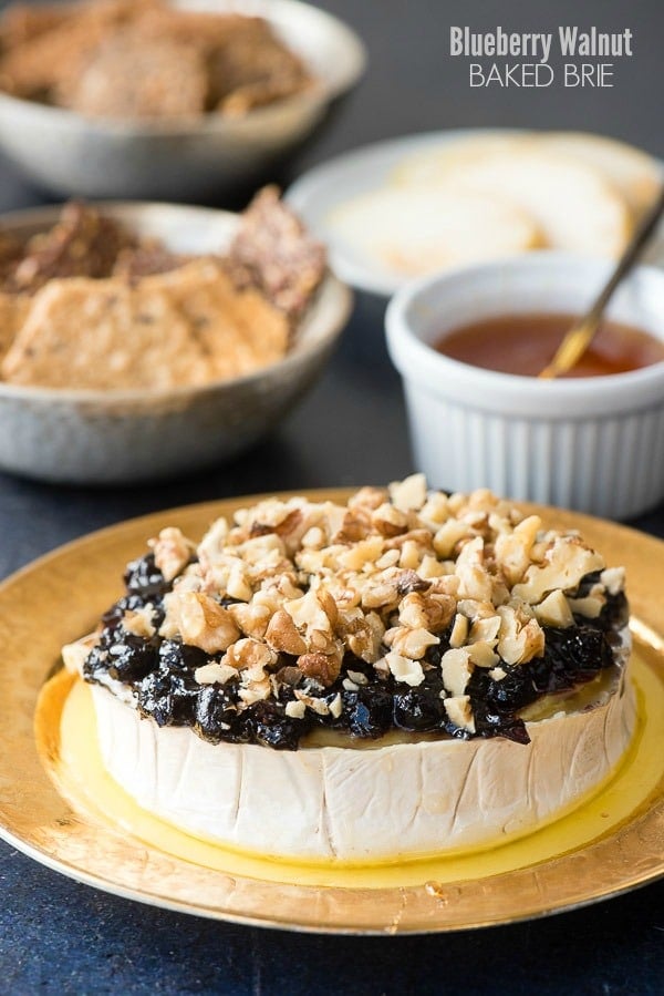 Blueberry Walnut Baked Brie with drizzled honey on an antique gold rimmed plate with gluten-free crackers