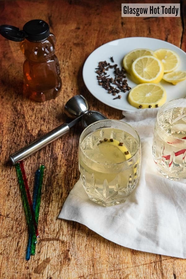 Glasgow Hot Toddy with clove-studded lemon slice in Waterford crystal etched glasses with a handled jigger