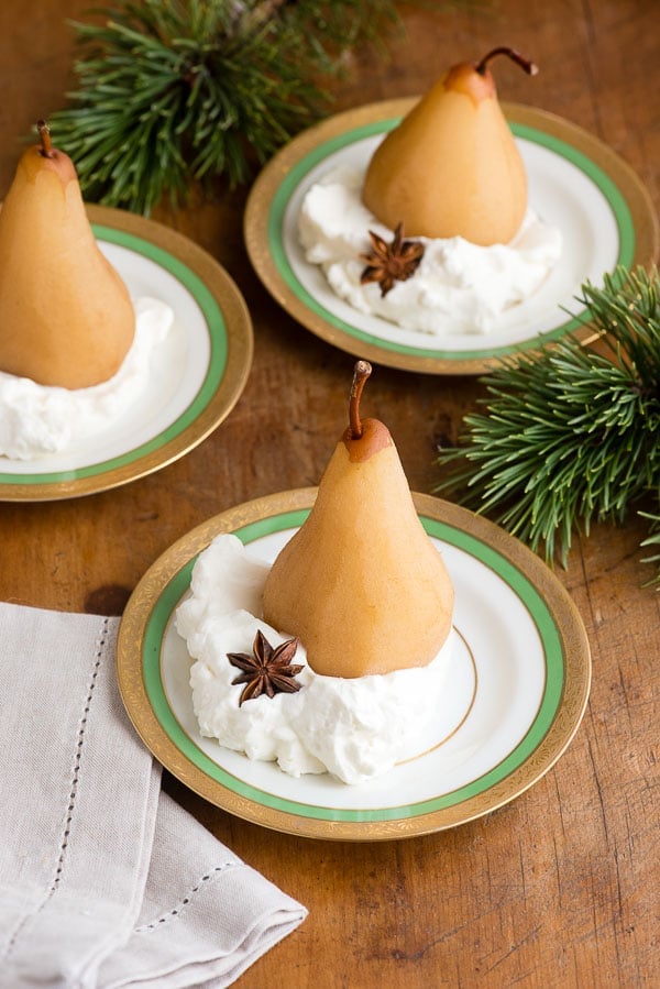 Spiced Chai Poached Pears sitting in freshly whipped cream on gold rimmed china plates with evergreen sprig