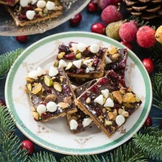 Gluten-Free Winter Cracker Toffee with cranberries, white chocolate chips, pistachio nuts, candied ginger and sea salt on a gold rimmed plate BoulderLocavore.com