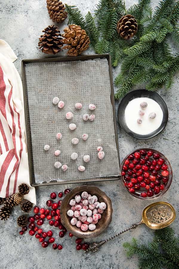 sugared cranberries in a bowl and on a baking sheet and some in process