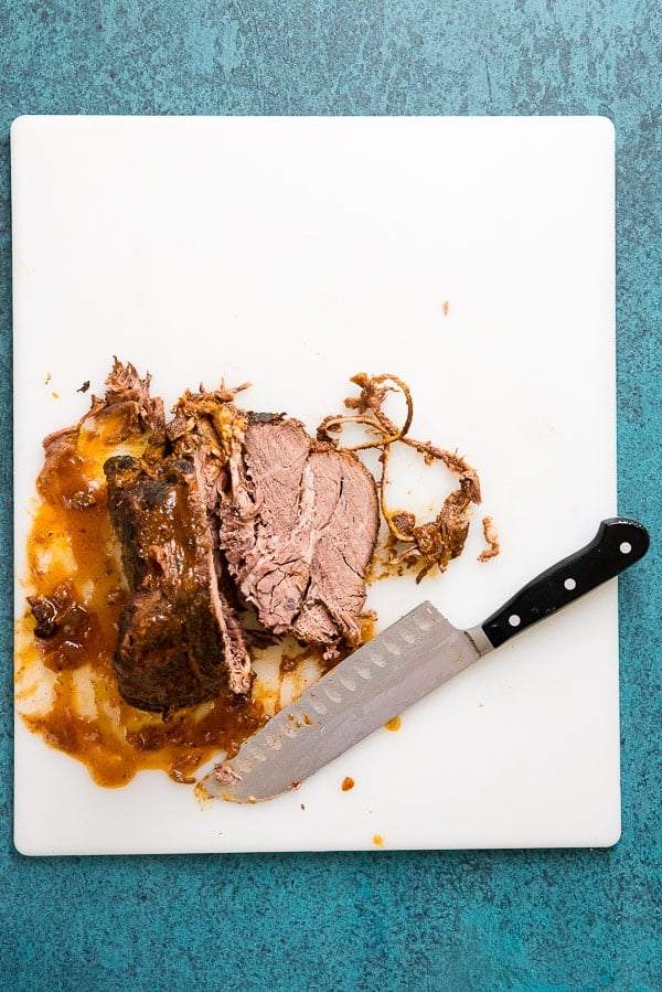 Slow Cooker Pot Roast sliced on a white cutting board with large knife 