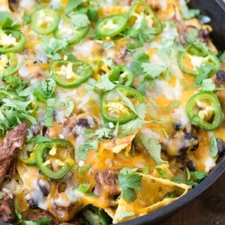 Spicy Pot Roast Nachos with melted cheese, sliced jalapenos in a cast iron skillet