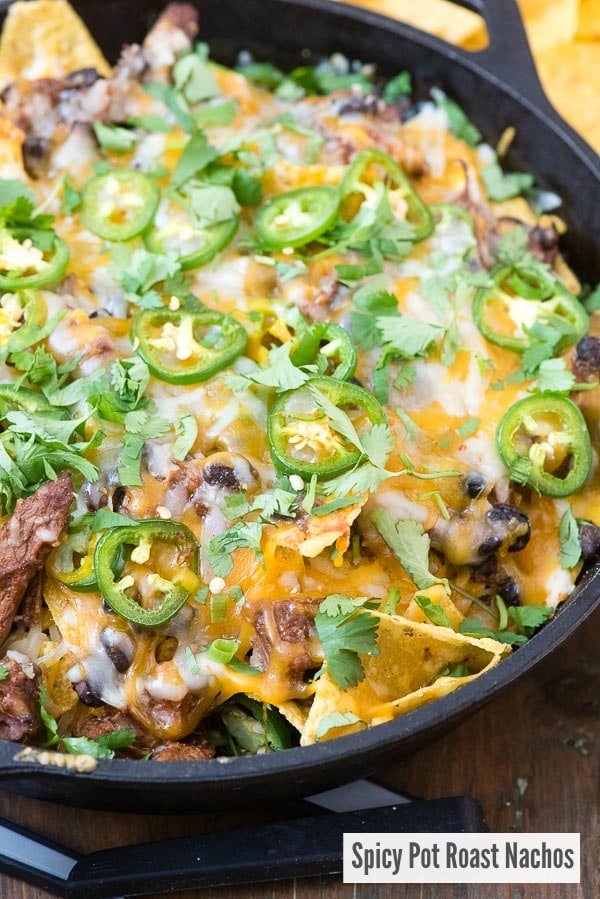 Spicy Pot Roast Nachos with melted cheese, sliced jalapenos in a cast iron skillet