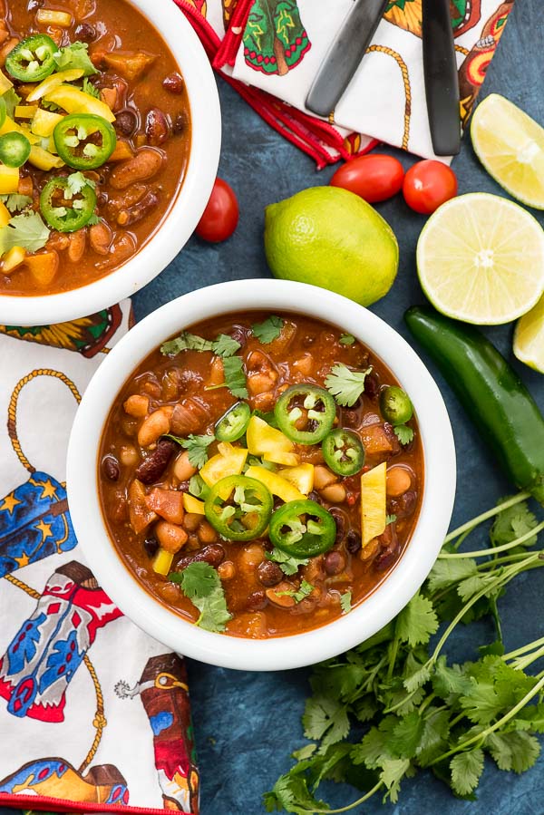 Hearty, quick to make Vegan Instant Pot Recipe: 4 Bean Chili with torn cilantro leaves, sliced jalapeno, diced yellow pepper in a white bowl