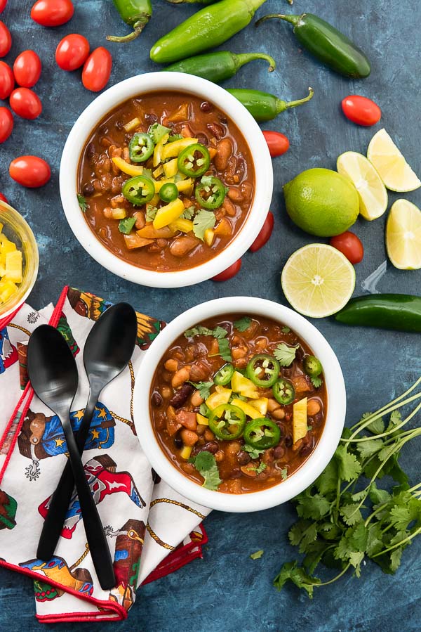Two hearty servings of Vegan Instant Pot Recipe: 4 Bean Chili with jalapenos, yellow bell pepper, cilantro in white bowls on a blue surface