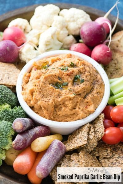 5-Minute Smoked Paprika Garlic Bean Dip in a white bowl with cut vegetables and crackers