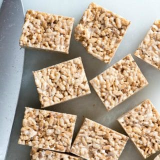 Gluten-free Brown Butter Rice Cereal Treat squares on a white cutting board with knife