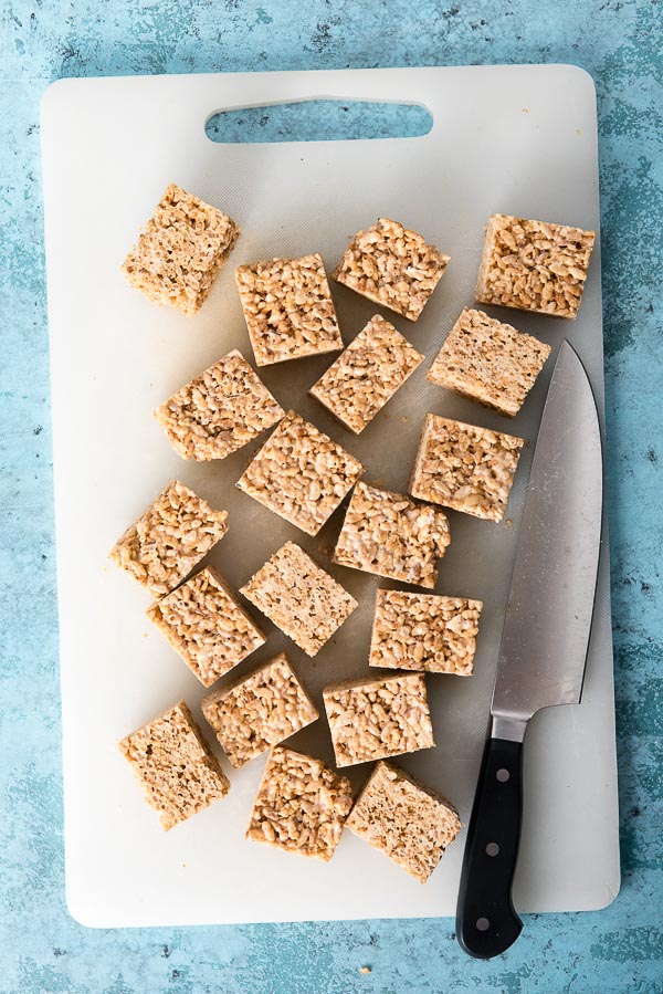 Fresh batch of Brown Butter Rice Cereal Treats cut into squares on white cutting board with knife