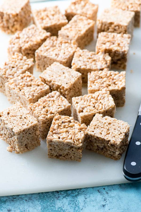 Brown Butter Rice Cereal Treats square cuts on a white cutting board with large knife