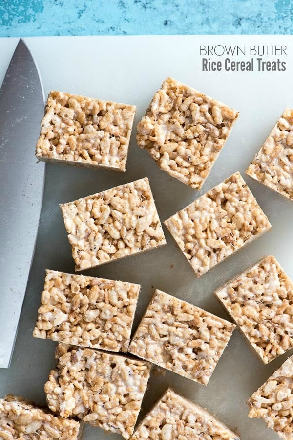 Gluten-free Brown Butter Rice Cereal Treat squares on a white cutting board with knife