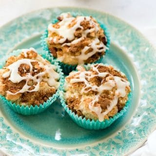 Three Coffee Cake Muffins with fresh orange glaze on a blue plate with flowered coffee cup