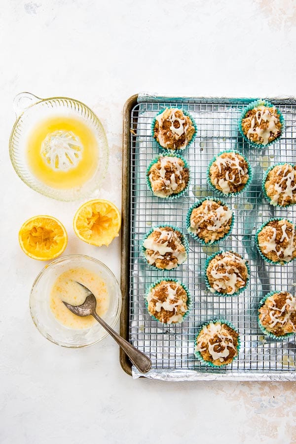 Baking sheet of coffee cake muffins with bowl of orange glaze and spoon