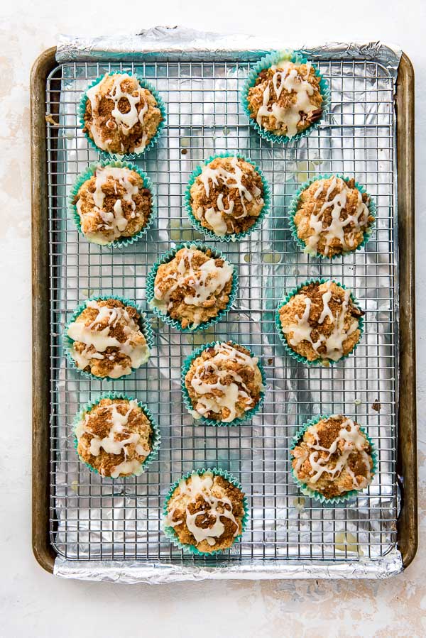 A batch of Coffee Cake Muffins freshly glazed on a cooling rack and baking sheet