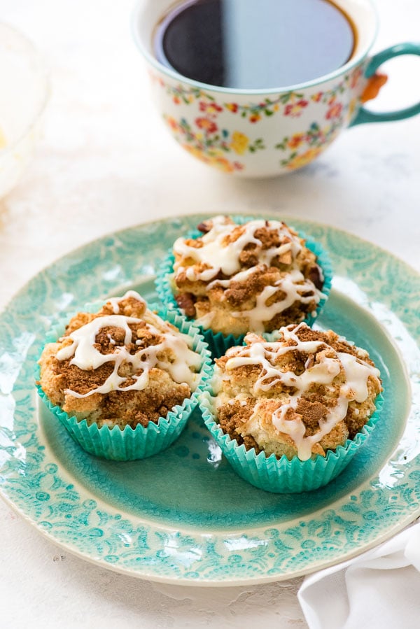 Three freshly baked gluten-free Coffee Cake Muffins with orange glaze on a blue embossed plate