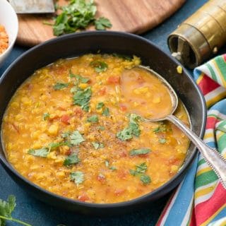 Curried Red Lentil Soup with torn cilantro in a black bowl with striped napkin