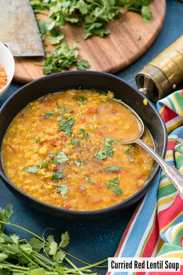 Curried Red Lentil Soup with torn cilantro in a black bowl with striped napkin