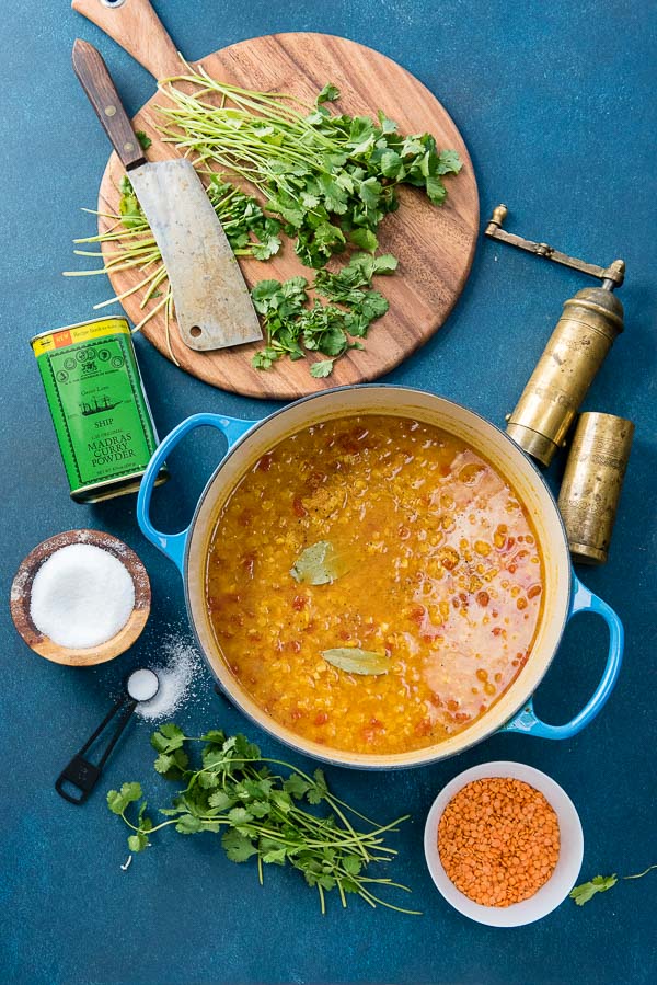 Blue enamel pot of Curried Red Lentil Soup with chopped cilantro, kosher salt pot, pepper grinder