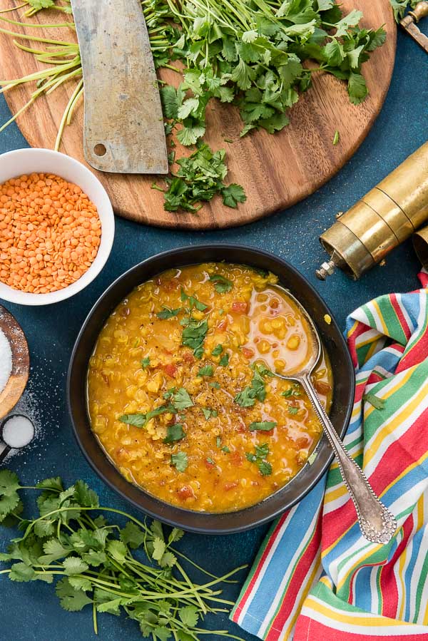 Steamy black bowl of Curried Red Lentil Soup with antique spoon, pepper grinder and striped napkin