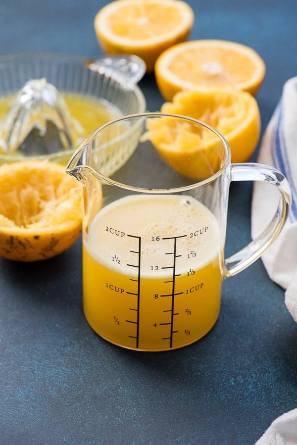 Freshly squeezed grapefruit juice in a glass measuring cup with glass juicer and grapefruit halves